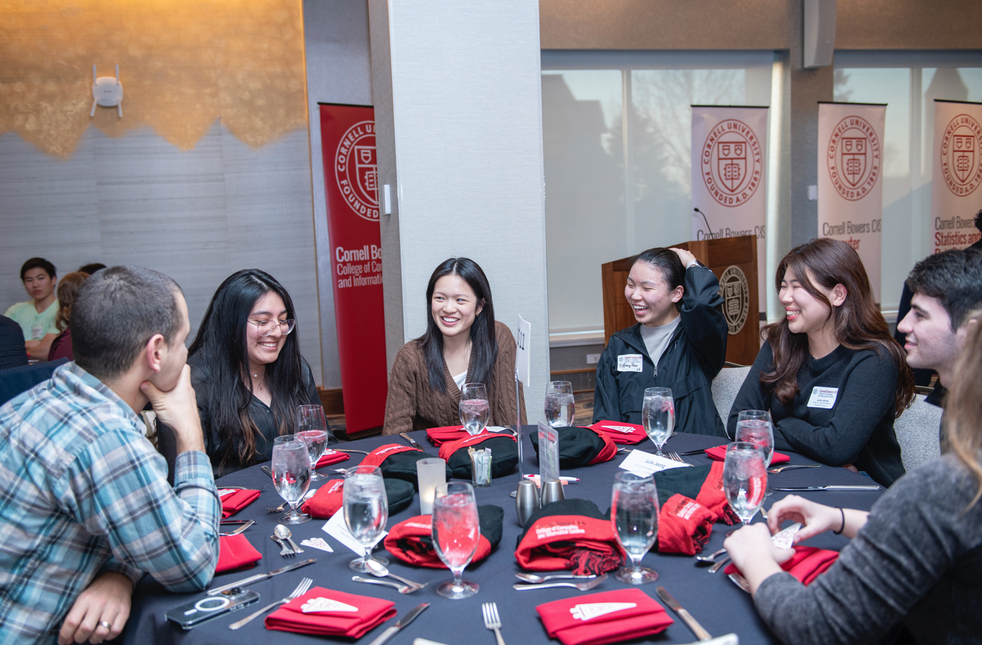 A color photo of people seated at a table, speaking to each other