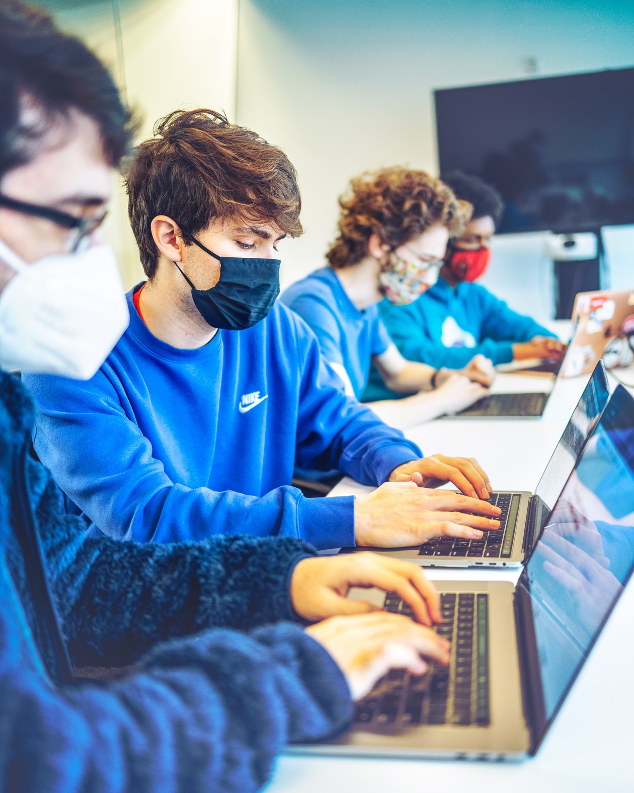 Two masked young men work at separate laptops